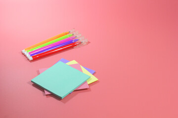 Pens and colored sheets on a pink background