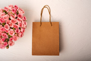 Bouquet of pink roses in the shape of a heart with a gift in a craft bag 