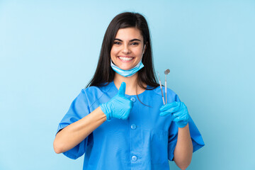 Young woman dentist holding tools over isolated blue background giving a thumbs up gesture