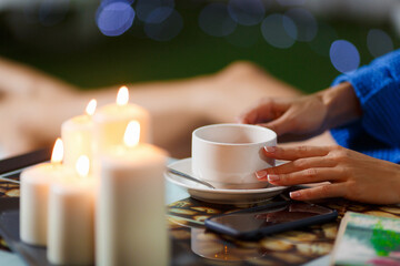 Woman in the spa salon lies on a lounger in a blue towel and a swimsuit. Relaxation and hot candles on the background. Enjoy an aromatic cup of black coffee.
