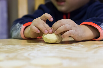 Baby hands sculpt dumplings from dough on a wood table