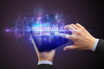 Businessman holding a foldable smartphone with BIOTECHNOLOGY inscription, new technology concept