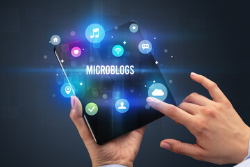 Businessman holding a foldable smartphone with MICROBLOGS inscription, social media concept