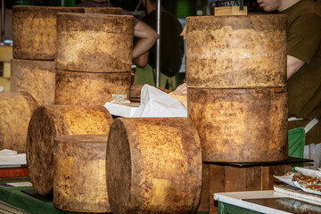 Giant cheeses in rounds piled on counter at market with unrecognizable workers in background - Selective focus