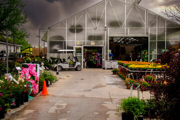 Commercial greenhouse on rainy spring day with lots of flowers and plants to sell and ATM parked outside on enclosure on wet pavement