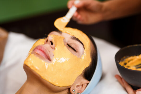 Procedure for skin care. Doctor in cosmetology office applies an yellow gold alginate mask to the face of young pretty woman.