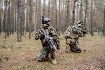 Portrait of a middle-aged bearded soldiers in a Woodland military uniform and helmet, with headphones on his head holding a rifle.