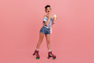 Lovely pinup girl posing on roller skates. Studio shot of amazed brunette woman with milkshake.
