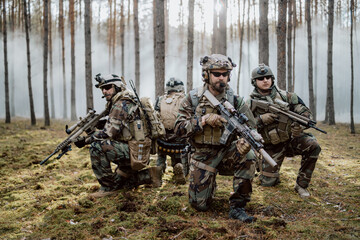 Four fully equipped, middle-aged soldiers in camouflage uniforms form a line, ready to fire, aiming...