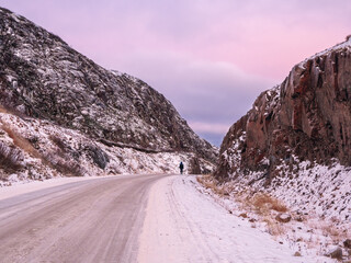 A snowy road stretching away into the distance between the hills. The magical purple color of dawn.