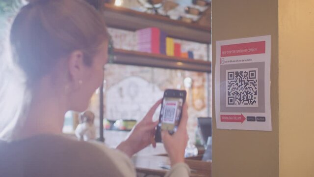 Woman with mobile phone checking into venue scanning QR code during health pandemic - shot in slow motion