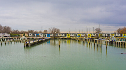 Fototapeta na wymiar Winter at the marina of an out-of-season beach resort near Grado, Friuli-Venezia Giulia, north east Italy. Chalets can be seen in the background which have been moved to temporary positions whilst inf