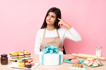 Pastry chef with a big cake in a table over isolated pink background making the gesture of madness...