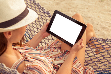 Woman holding a tablet computer while sitting in a hammock on the beach