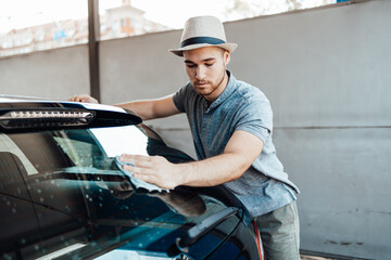 Young handsome man with hat cleaning car with rag, car detailing (or valeting) concept.