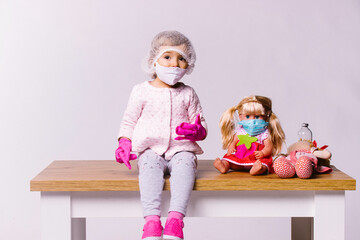Little girl in a medical mask and pink latex gloves with toys on a white background. Pediatric clinic and approach to young patients.