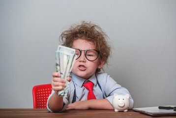 Fototapeta na wymiar Funny angry kid boss with money. Portrait of angry displeased little child with freckles isolated over white background wearing glasses and suit. Child clenches money in a fist