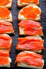 Bruschettes with butter and red fish on a black wooden board.