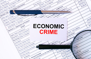 Obraz premium Business card with text Economic Crime lying on financial tables with a pen and magnifying glass