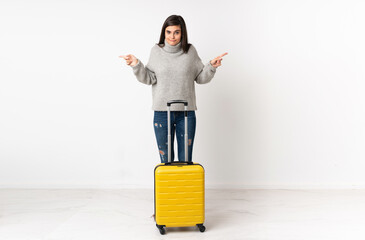 A full length body of a traveler woman with a suitcase over isolated white wall pointing to the laterals having doubts