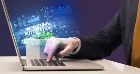 Businessman working on laptop with MARKETING AUTOMATION inscription, cyber technology concept