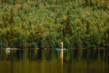 Man rowing oar on sup board blue lake water paddleboard background of forest