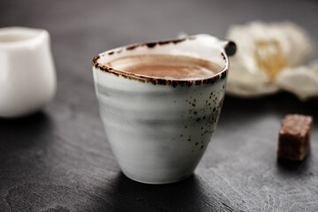 Ceramic coffee mug with coffee with milk or latte, sugar cubes on dark background. Rustic breakfast concept. Side view.