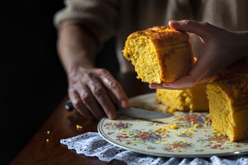 Female hand holds up a slice of cake. With the other hand she holds a knife.