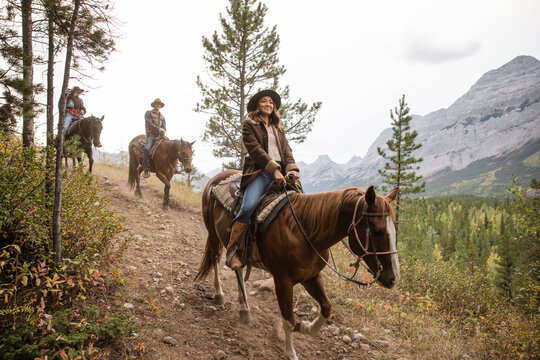 Happy young woman horseback riding on trail in scenic mountains