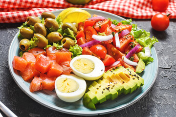 Ketogenic, paleo diet lunch bowl with salted salmon fish, lemon, avocado, olives, boiled egg, tomato, green lettuce salad, healthy food