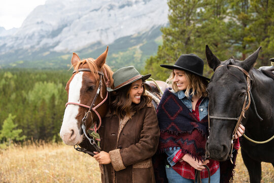 Happy Young Women Friends Horseback Riding In Mountains