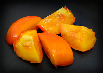 sliced ripe and juicy fruit of a sharon on a black background