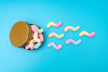 Sugar coated jelly worms crawling out of a round tin box on a blue background