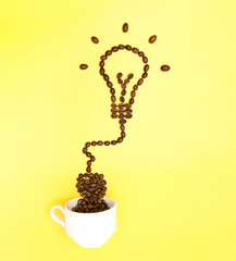 Creative arrangement of roasted coffee beans resembling a glowing light bulb plugged to a white...