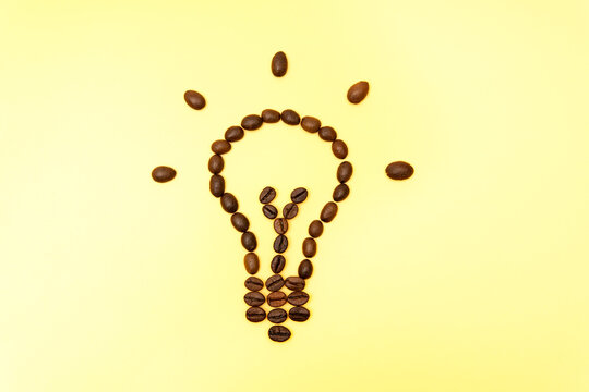 Glowing light bulb shape made of coffee beans on yellow background