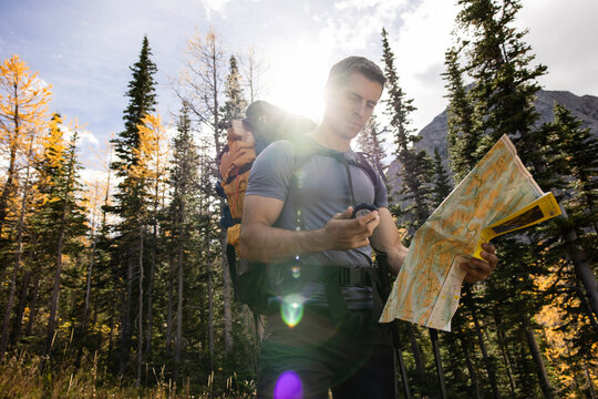 Male backpacker using map and compass in sunny autumn woods