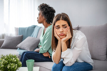 Two friends not talking to each other after fight on the sofa in sitting room at home. Two upset friends not talking to each other after fight on the sofa in sitting room at home