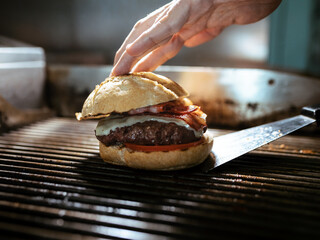 Hand's chef preparing delicious burger on grilled in the restaurant kitchen.