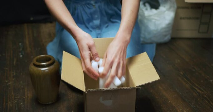 A young woman is packing a vase in a box with styrofoam balls before putting it in a bigger moving box