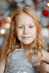 Fototapeta premium A large portrait of a little girl with curly orange hair. She looks at the camera