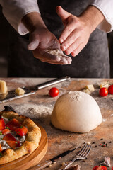 Chef preparing pizza dough at home or in the kitchen. A cloud of flour in the air. Hands close up.