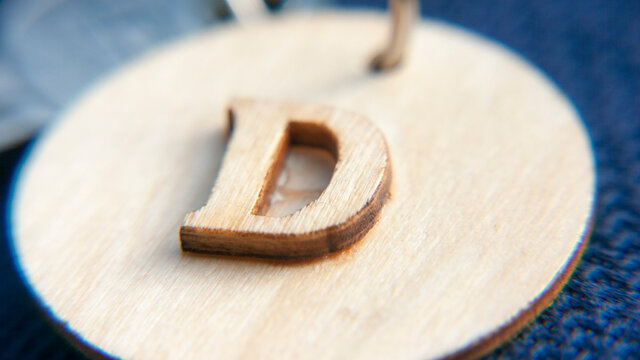 Letra d tallada en madera pegada con pegamento sobre chapa redonda de madera de llavero