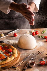 Chef preparing pizza dough at home or in the kitchen. A cloud of flour in the air. Hands close up.