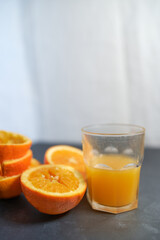 Glass of squeezed orange juice and peels, on gray table.