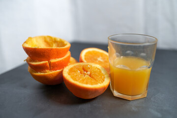 Glass of squeezed orange juice and peels, on gray table.