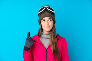 Teenager skier girl with snowboarding glasses over isolated blue background pointing with the index finger a great idea