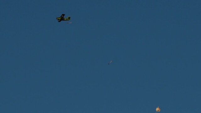 A group of paratroopers leaves the plane one by one.
The paratroopers are jumping from a light single-engine An-2 biplane in the cloudless blue sky. 