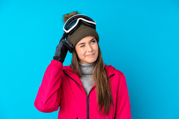 Teenager skier girl with snowboarding glasses over isolated blue background having doubts and with confuse face expression