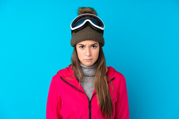 Teenager skier girl with snowboarding glasses over isolated blue background sad