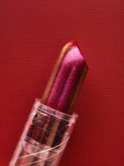 Closeup of new tube of shiny lipstick on red. Sophisticated red make up sample. Minimalist makeup and cosmetics background. Trendy colour, beauty, shopping, sale concept. 
